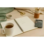 Bureau de créatrice avec carnet, calculatrice et tasse de thé – calcul du chiffre d’affaires idéal